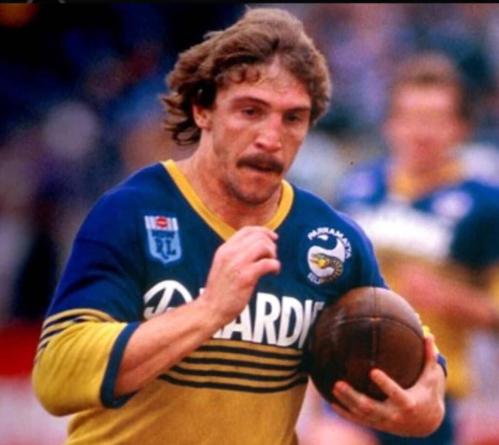 EILMELDUNG NACHRICHTEN: Rugby-League-Legende Brett Kenny, der Maestro der Parramatta Eels, zählt zu den größten Spielern, die dieser Sport je hervorgebracht hat. Berühmt für seine brillante Kreativität, sein außergewöhnliches Spielverständnis und seine Fähigkeit, Spiele im Alleingang zu entscheiden, dominierte Kenny sowohl national als auch international … mehr dazu 👇🏿